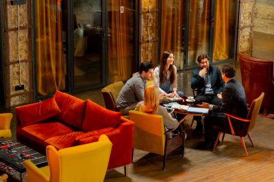 Quatre personnes discutent dans un espace de coworking moderne avec fauteuils colorés et table basse