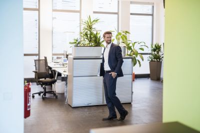 Un homme en costume dans un espace de bureau moderne avec des plantes et des meubles design.