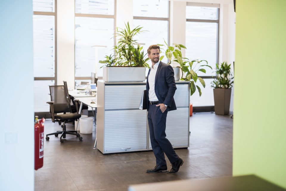 Un homme en costume dans un espace de bureau moderne avec des plantes et des meubles design.