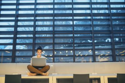Jeune femme assise sur un banc, travaillant sur un ordinateur portable dans un espace de coworking lumineux.