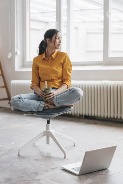 Femme assise sur un tabouret ergonomique, buvant une boisson verte dans un espace de coworking lumineux