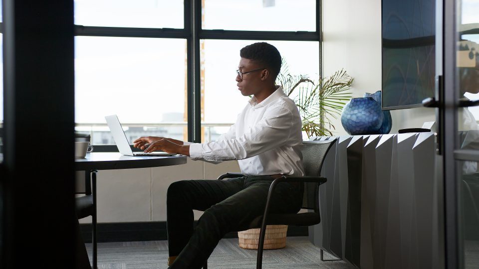Jeune professionnel en chemise blanche travaillant sur un ordinateur dans un espace de coworking moderne et lumineux.