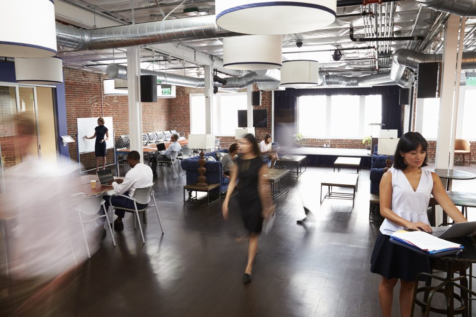 Espace de coworking avec briques apparentes, tables hautes et collaborateurs en mouvement