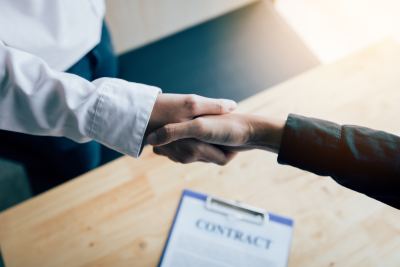 Deux personnes se serrent la main dans un bureau, avec un contrat sur la table