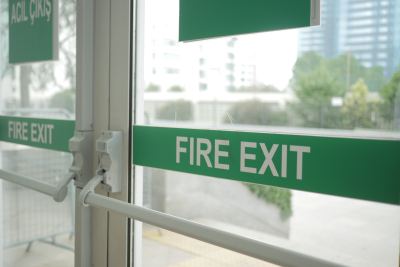 Porte vitrée avec signalétique bilingue 'FIRE EXIT' et 'ACIL ÇIKIŞ', équipée d'une barre antipanique