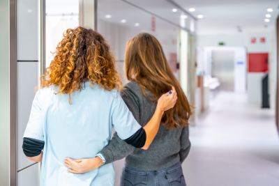 Deux femmes, dont une en blouse médicale, discutent dans un couloir propre et bien éclairé d'un établissement de santé.