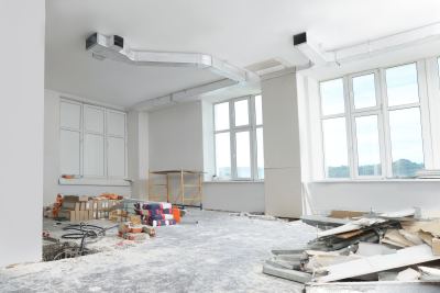 Espace de bureau en rénovation avec murs blancs, grandes fenêtres et matériaux de construction dispersés.