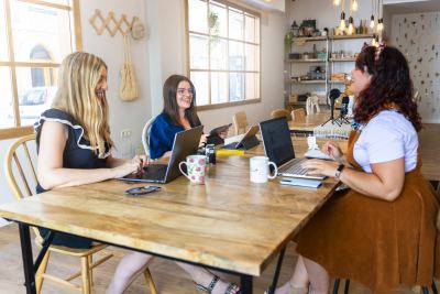 Trois femmes discutent autour d'une table en bois dans un espace de coworking lumineux et décoré.