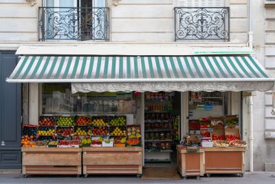 Façade d'un commerce de rue avec auvent vert et blanc et étals de fruits et légumes frais