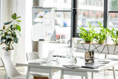 Table blanche entourée de chaises design dans un espace de coworking lumineux avec plantes et vue extérieure.