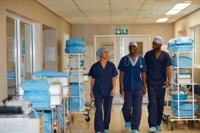 Trois membres du personnel médical en tenues bleues avancent dans un couloir d'hôpital bien organisé.