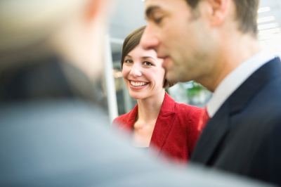 Femme en blazer rouge discutant avec deux hommes en costume dans un espace de coworking
