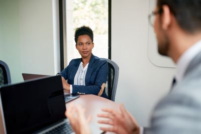 Femme en blazer bleu discutant avec un collègue dans un espace de travail lumineux