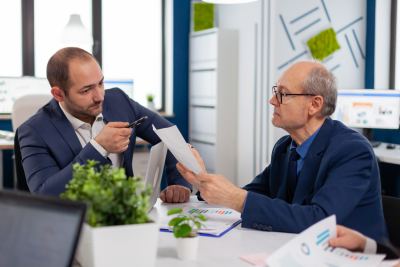 Deux professionnels en costume discutent autour de documents dans un espace de travail moderne.